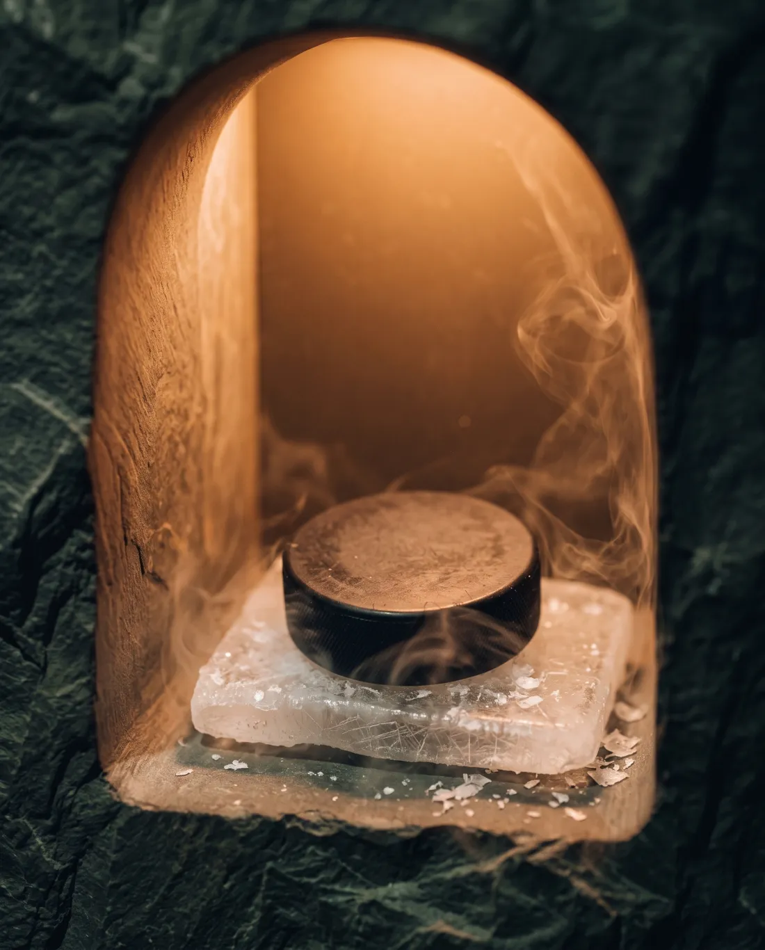 A black hockey puck on a slab of frosted rink ice inside a warmly lit stone niche