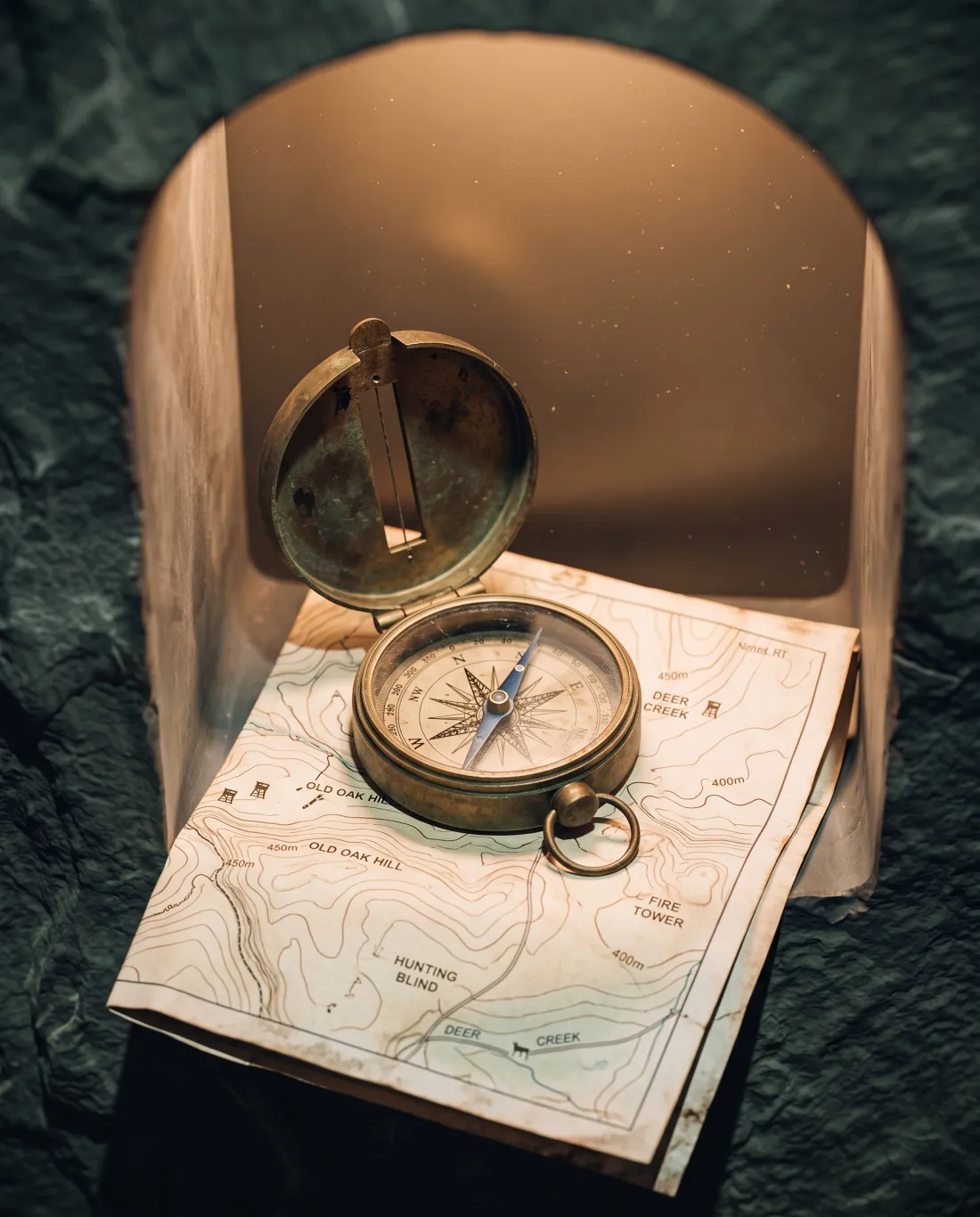 A brass field compass resting on a topographic hunting map inside a lit stone niche